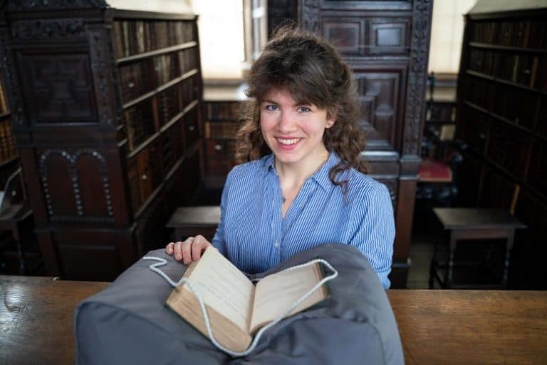 LAURA VAN HOLSTEIN IN THE OLD LIBRARY AT ST JOHN'S COLLEGE, CAMBRIDGE, WITH A FIRST EDITION OF CHARLES DARWIN'S SEMINAL BOOK ON THE ORIGINS OF SPECIES