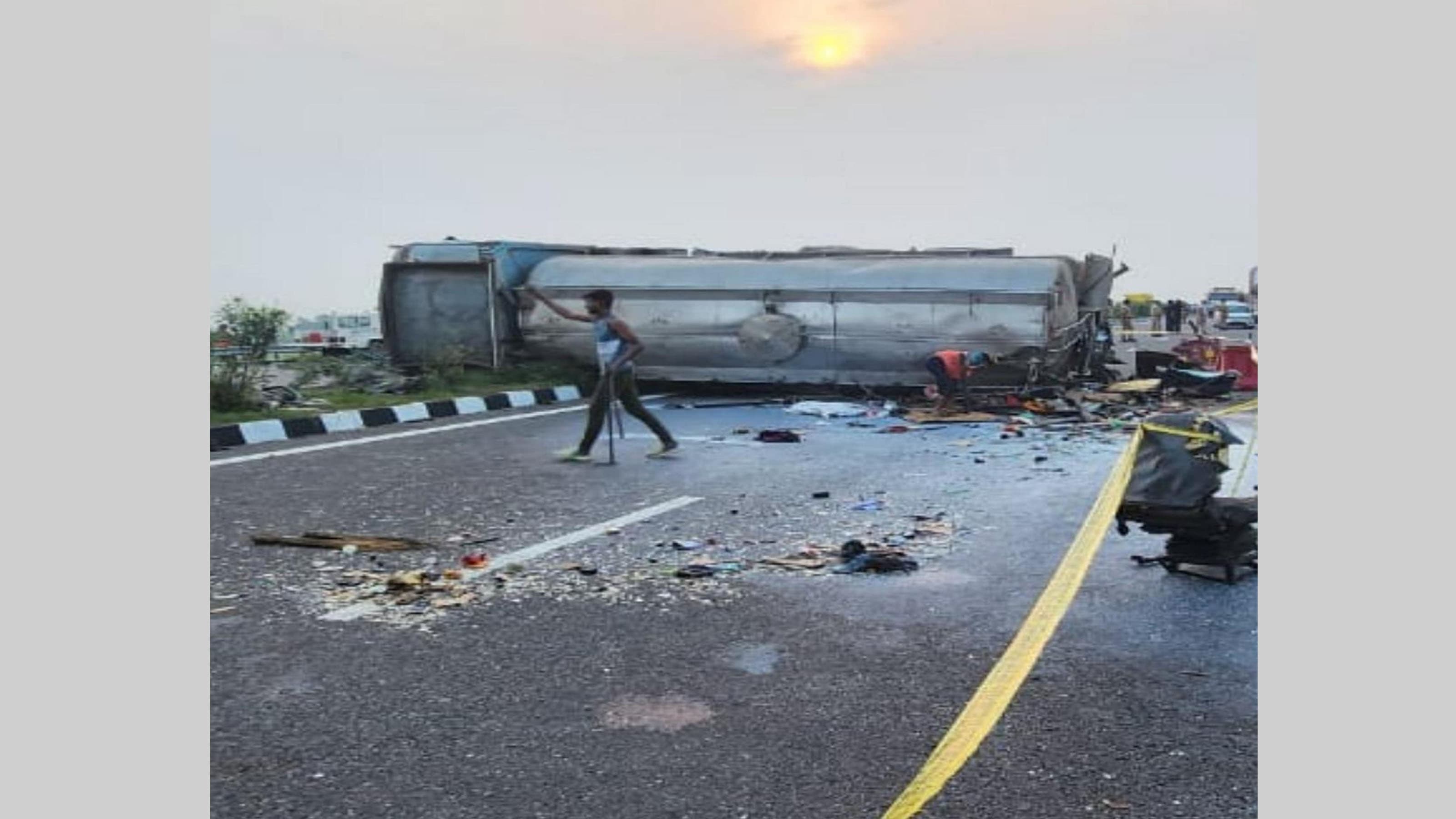 People stand near an overturned vehicle after an accident, in Unnao district, on July 10, 2024. At least 18 people were killed and 19 injured when a bus collided with a tanker on the Agra-Lucknow Expressway in the Uttar Pradesh district.