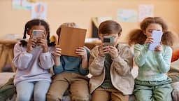 Schoolchildren using a smartphone together in a school corridor, highlighting children's internet access, social media use and online safety.